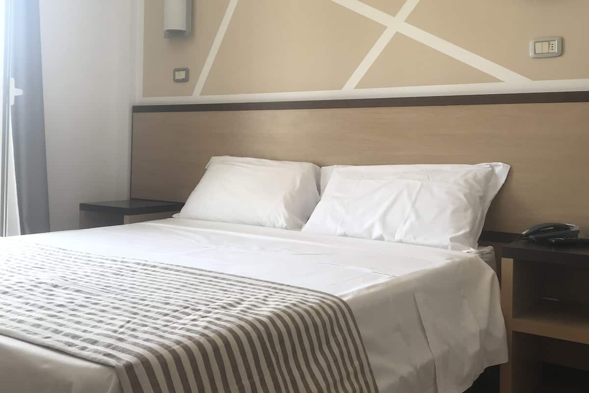 Una habitación de hotel con una cama, dos mesitas de noche, una lámpara de pared y un enchufe.
