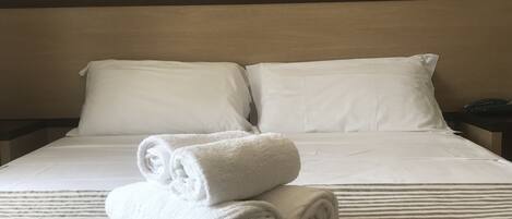 A neatly made bed with white linens and rolled towels on a striped bedspread.