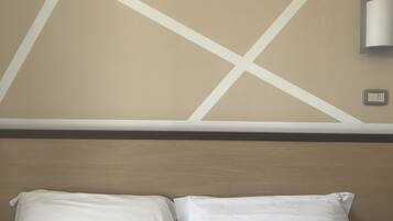 Habitación de hotel con cama, dos almohadas, cabecero y lámpara de pared.