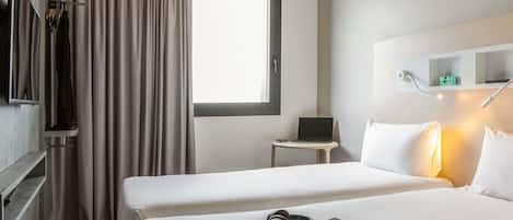 A hotel room with two beds, a desk with a laptop, a TV, and a window with curtains.