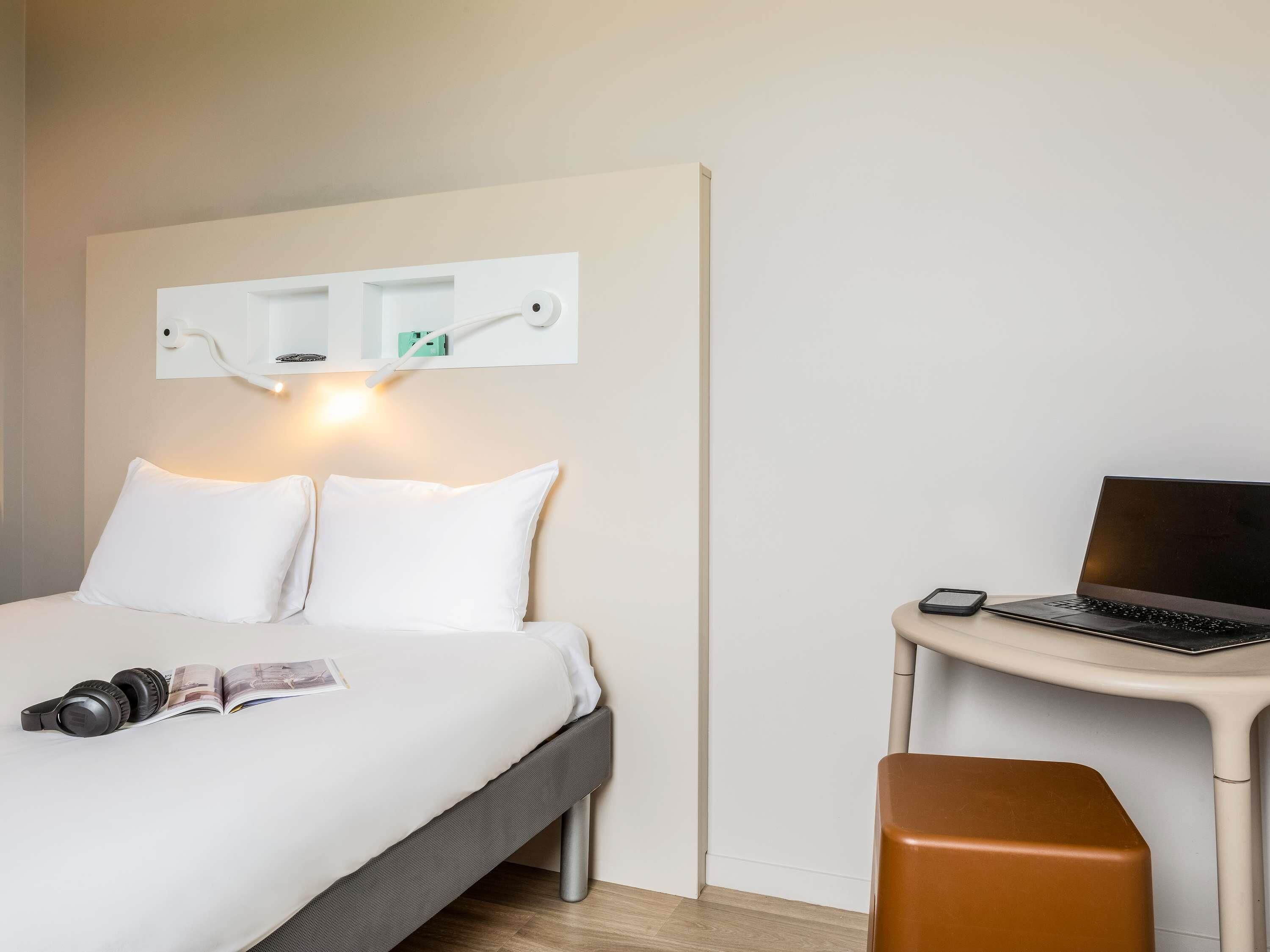 Una habitación de hotel con una cama, un escritorio con una computadora portátil, una silla y una mesita de noche.