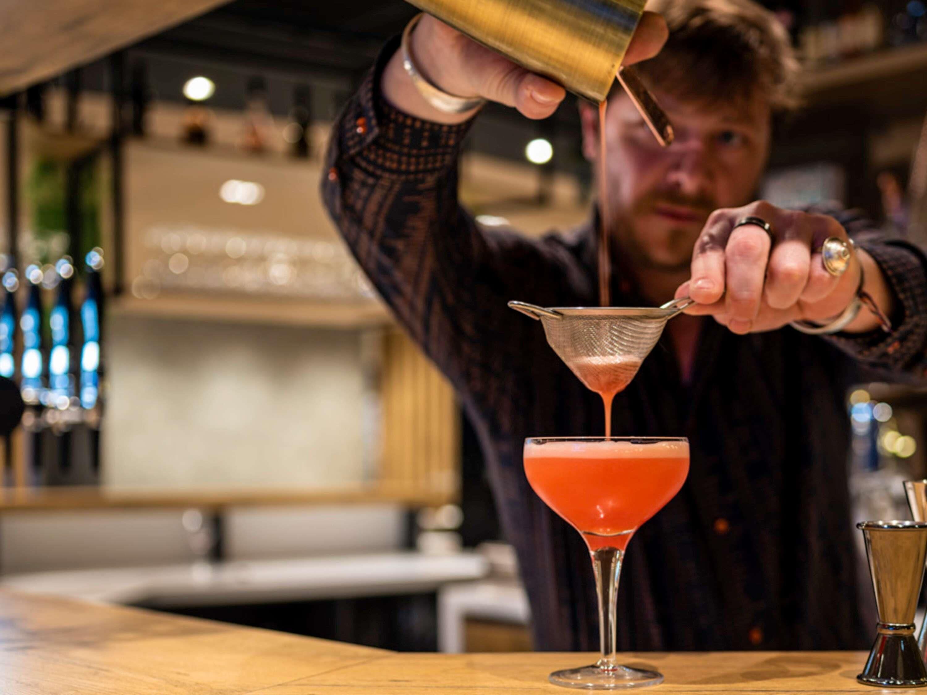 A bartender pouring a drink into a martini glass.