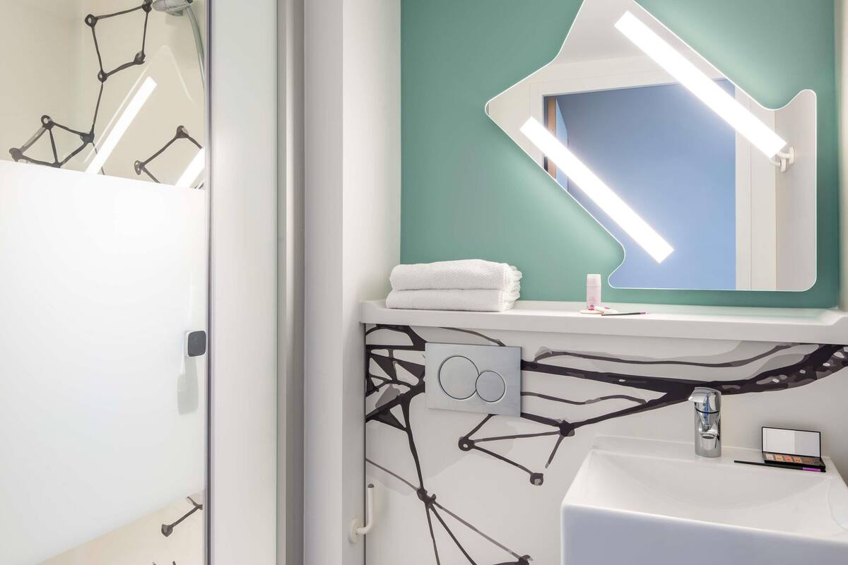 A bathroom with a white sink, a mirror with a teal accent wall, and a shower area with a curved design.