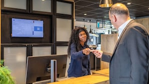 A reception desk with a computer monitor displaying a document, a wooden counter, and a modern interior design. - ibis budget Gonesse Le Bourget (Gonesse)