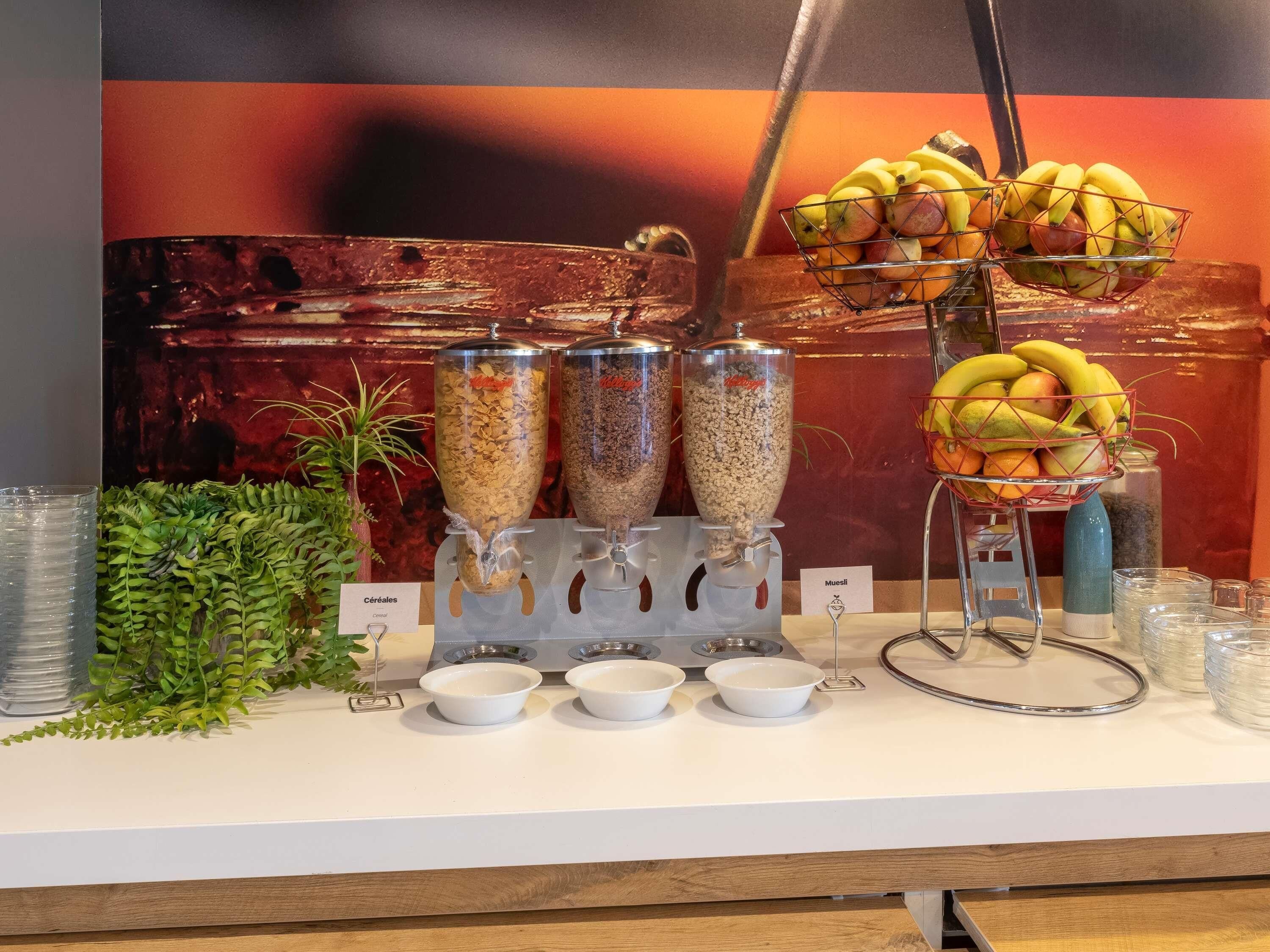 Montaje de bufé con dispensadores de cereales, tazones y una cesta de frutas.