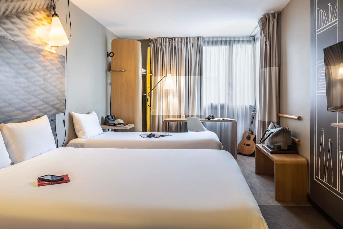 A hotel room with two beds, a desk, a guitar, and a TV.