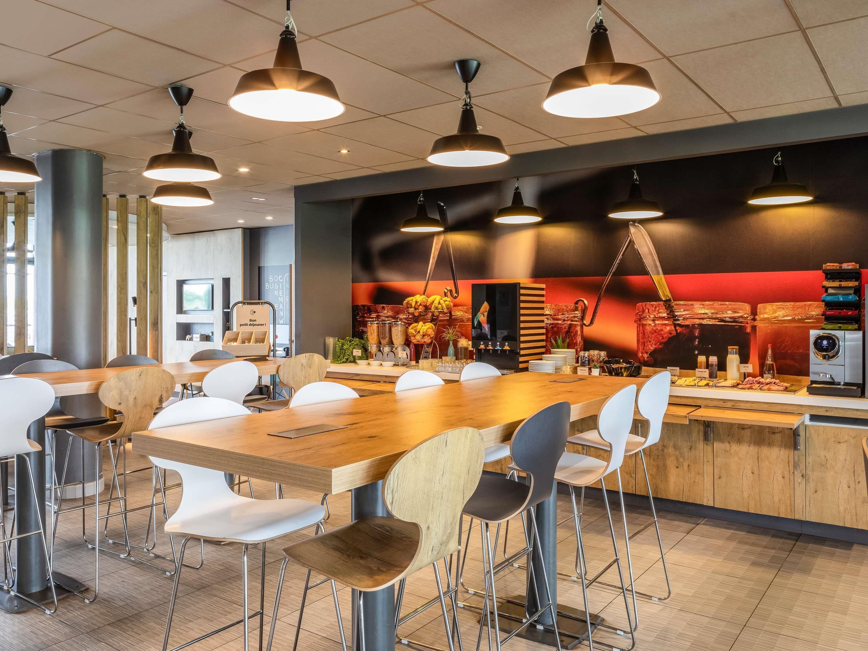 A modern dining area with a long wooden table, white and brown chairs, and pendant lighting.
