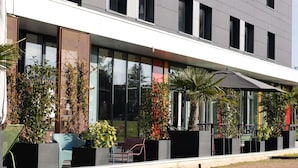 Un edificio moderno con grandes ventanales, asientos al aire libre y plantas en macetas.