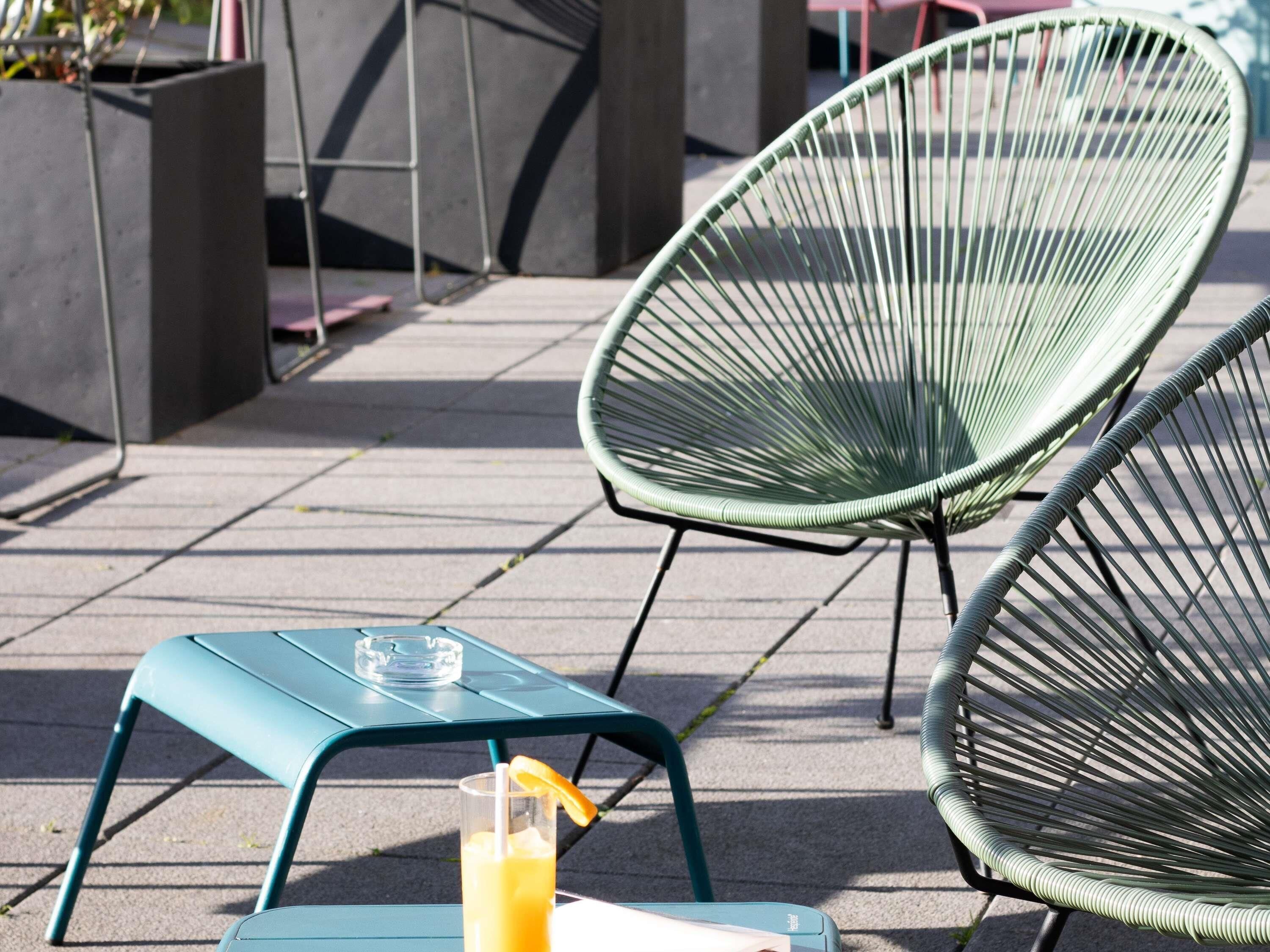 Outdoor seating with metal chairs and a table, a drink with a straw and a lemon wedge, and a clear glass.