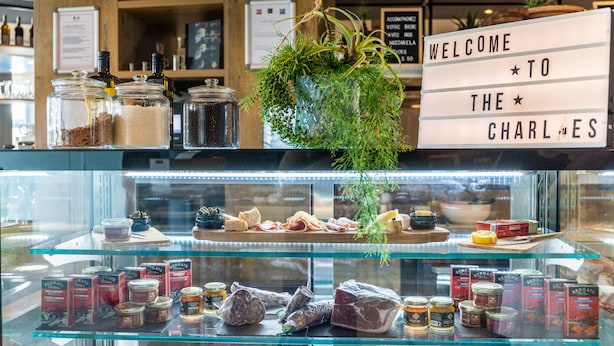 Mostrador de delicatessen con un cartel que dice “WELCOME TO THE CHARLES” y varios productos expuestos.