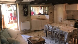 A cozy kitchen with a dining table, chairs, a clock, and a window overlooking a garden. - Gîte 5p, 3*, Lascaux Périgord Noir, wifi parc Spa piscine chauf ok dog & cat (Montignac-Lascaux)