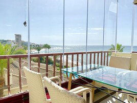 Un balcone con un tavolo in vetro e sedie in vimini, con vista su una spiaggia e l'oceano.