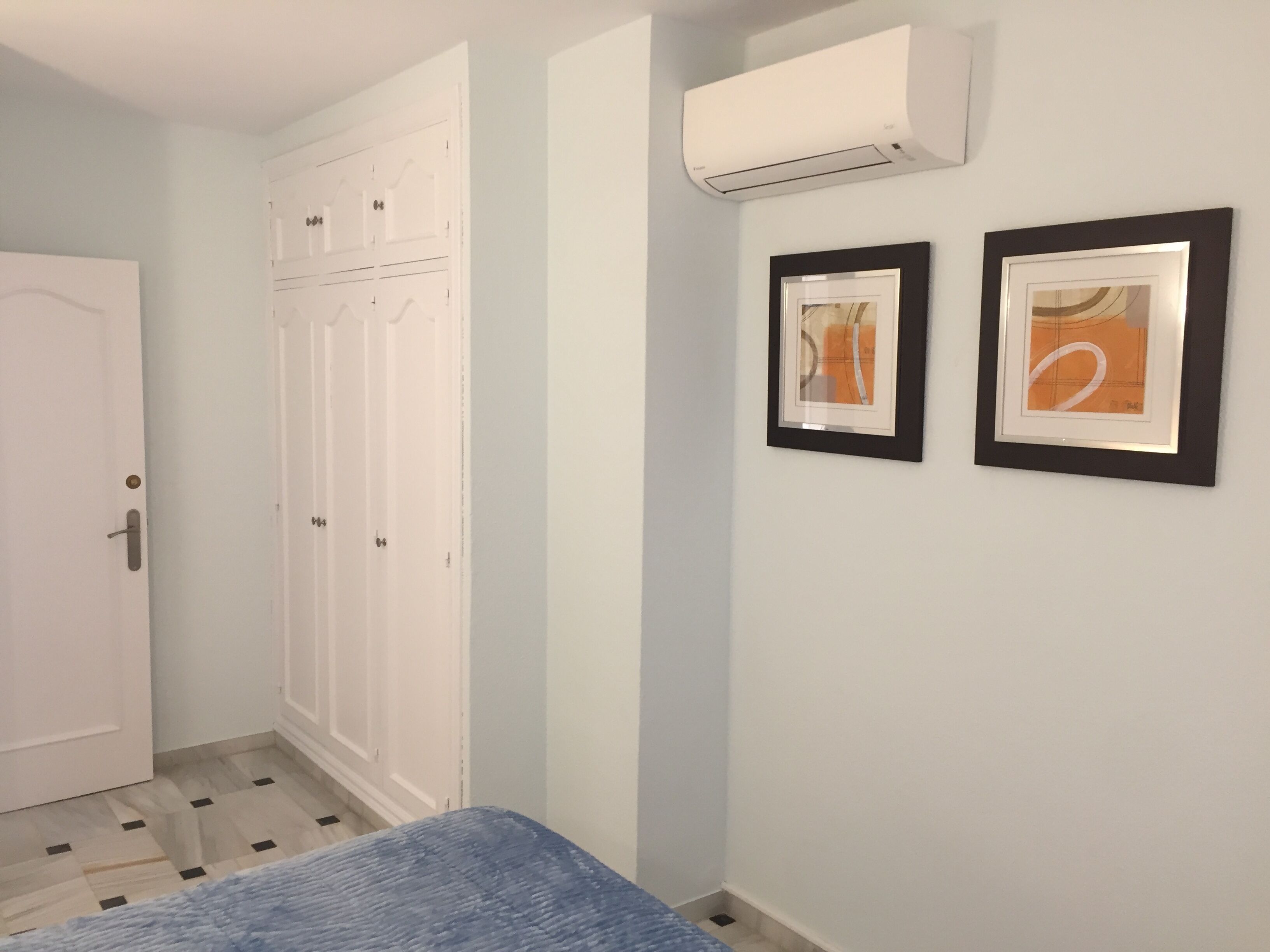 A bedroom with a bed, a wardrobe, and two framed pictures on the wall.