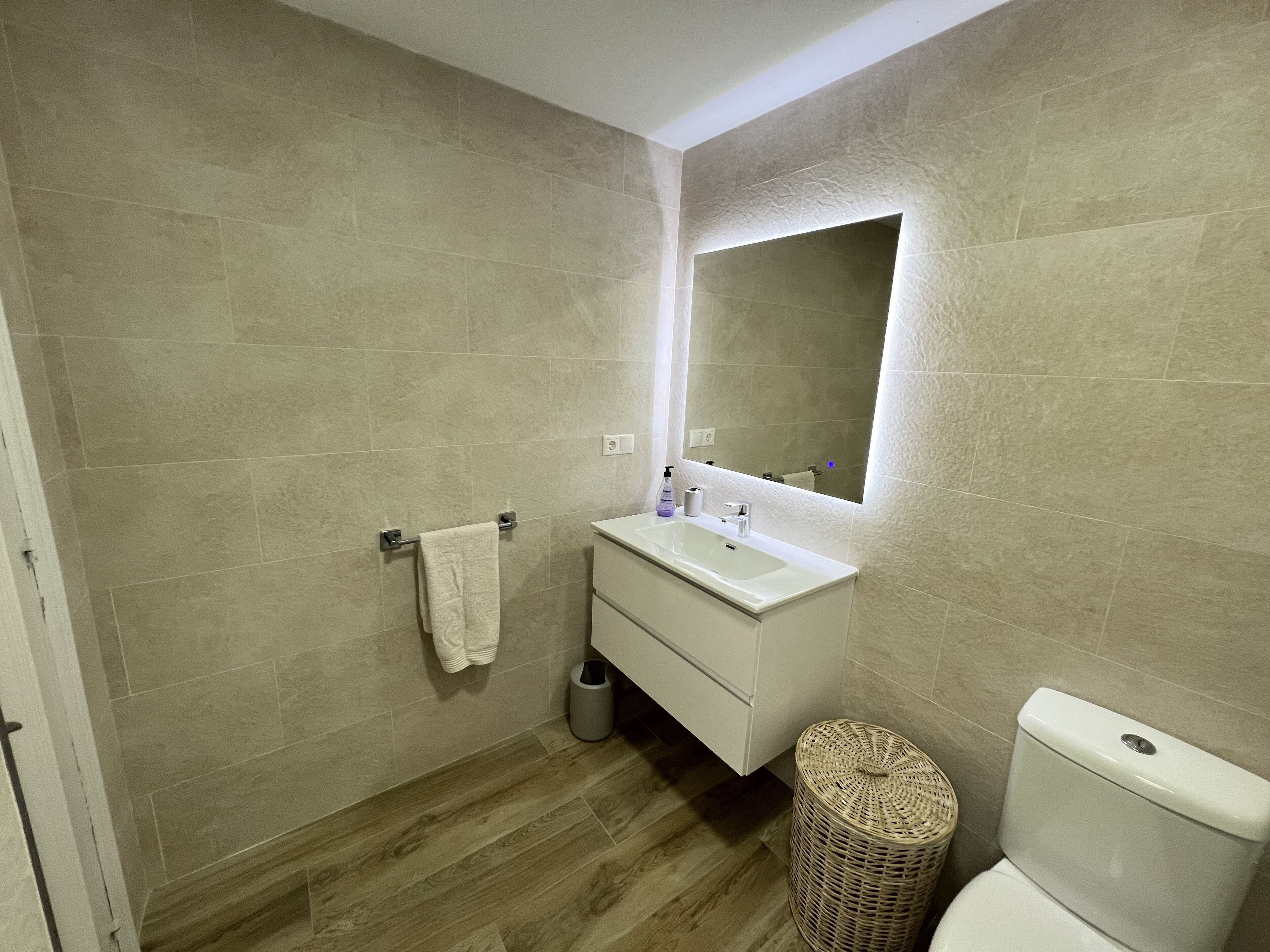 Une salle de bain avec un plancher en bois, un lavabo blanc, un miroir et des toilettes.