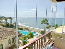 Vista da un balcone su una spiaggia, una piscina e un cielo azzurro terso.