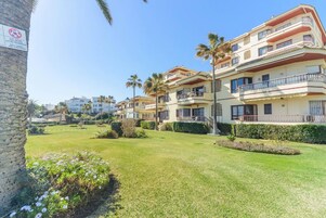 A residential building with multiple balconies, a well-maintained lawn, and palm trees.