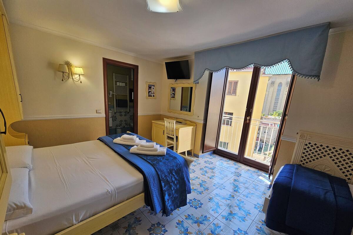 Ein Hotelzimmer mit Bett, Schreibtisch, Stuhl, Fernseher und einem Balkon mit Aussicht.