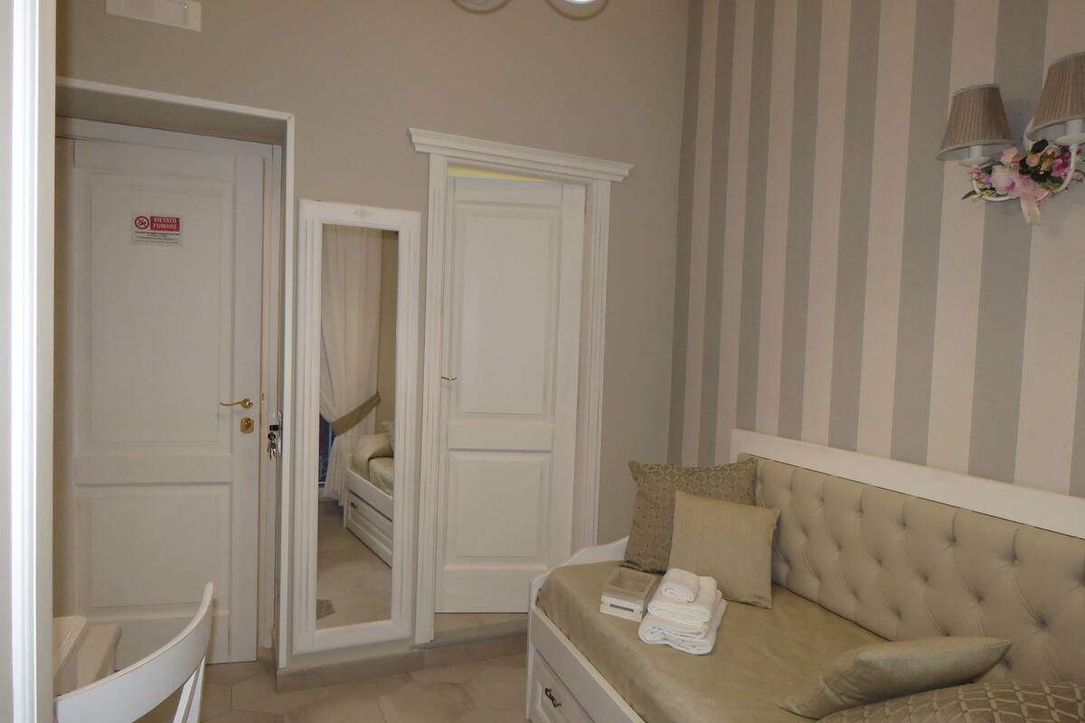 Ein Schlafzimmer mit einem Bett, einem Nachttisch, einem Spiegel, einem Kleiderschrank und einer gestreiften Wand.