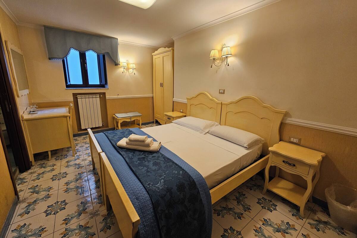 Ein ordentlich eingerichtetes Schlafzimmer mit Bett, Nachttischen, Schreibtisch und Fernseher.