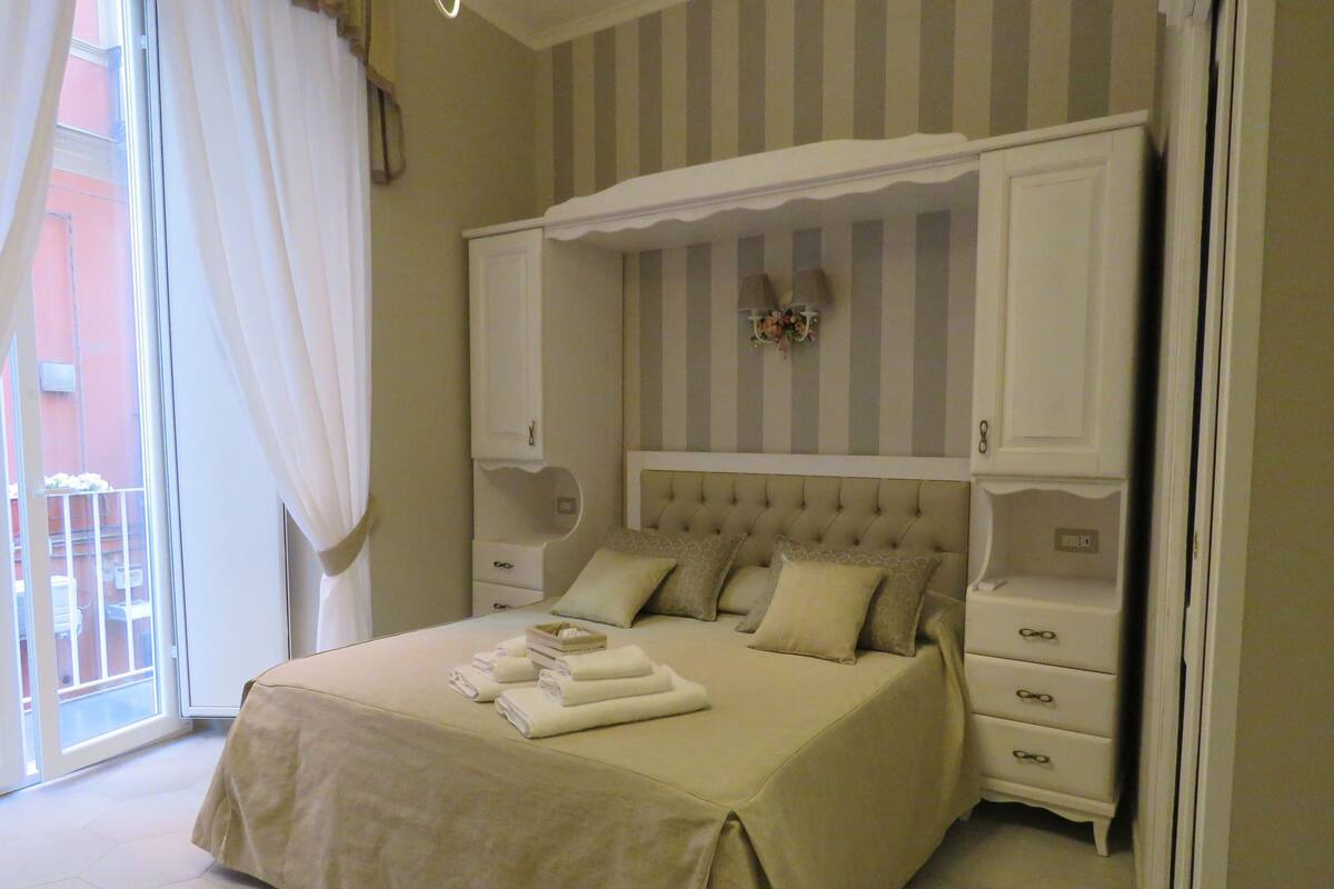 Ein Schlafzimmer mit Bett, Nachttisch, Kommode und einem Fenster mit Vorhängen.
