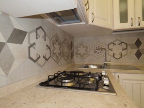 A kitchen with a gas stove, a sink, and decorative wall tiles. - Le Ninfe Luxury Rooms (Naples)
