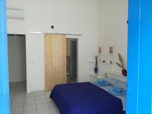 Un dormitorio con cama, puerta de madera, baño y estante con adornos.