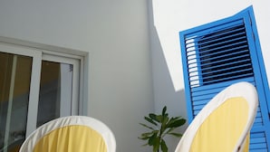 A white building with a blue window shutter, two white chairs with yellow cushions, and a potted plant. - Mediterranea Guesthouse B&B (Portopalo di Capo Passero)