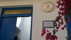 A blue door leading into a room with a wall-mounted fan and a sign with contact information. - Mediterranea Guesthouse B&B (Portopalo di Capo Passero)
