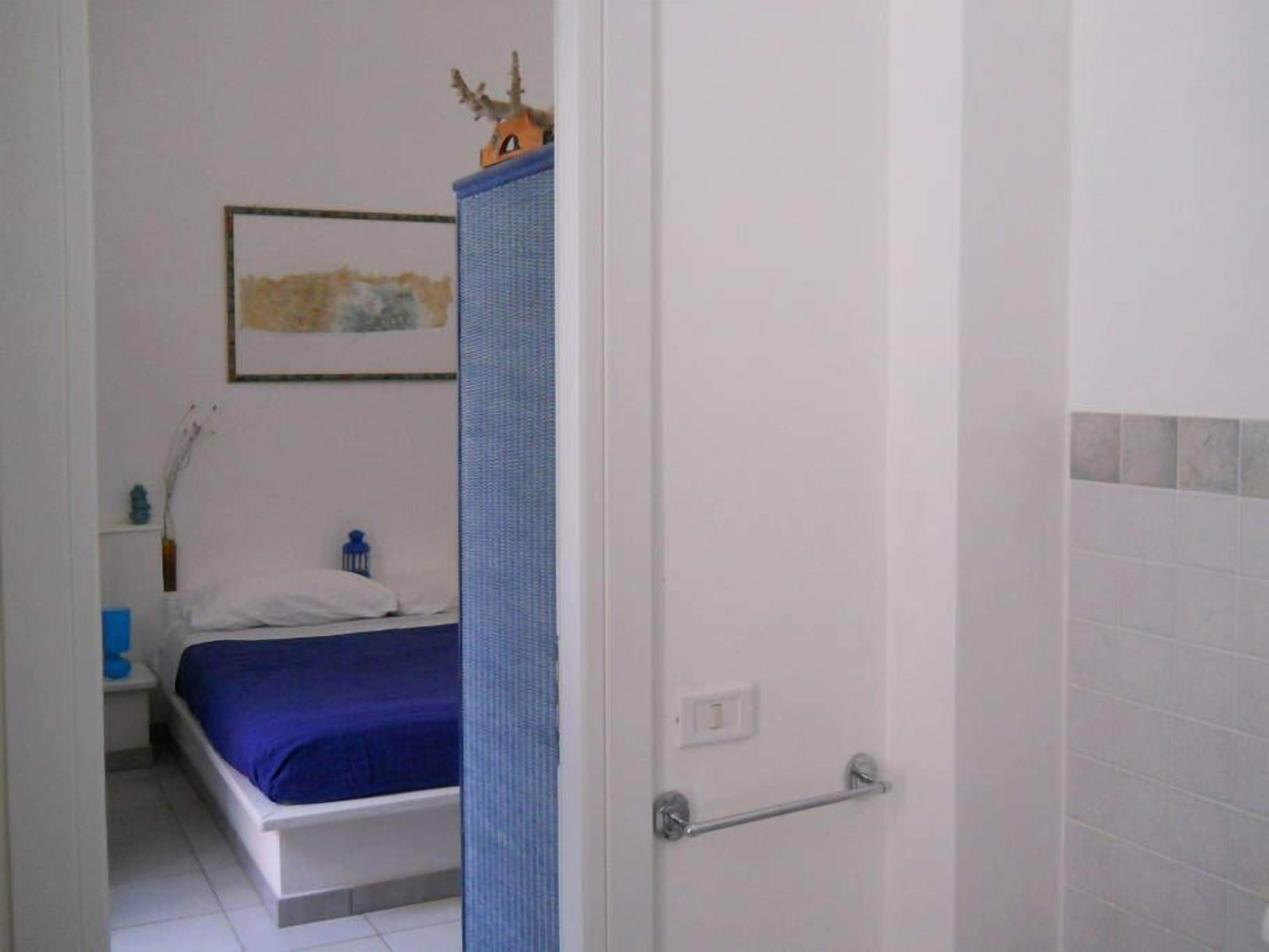 Un dormitorio con cama, mesita de noche, toalla azul, un cuadro en la pared y puerta de baño.
