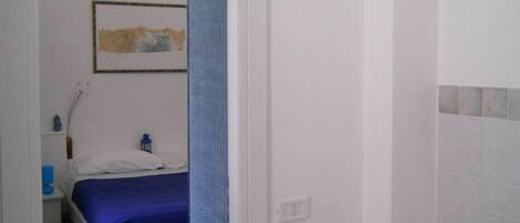 Un dormitorio con cama, mesita de noche, toalla azul, un cuadro en la pared y puerta de baño.