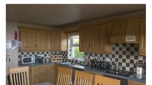 A compact kitchen with wooden cabinets, a microwave, a toaster, and a sink. - Beachview Cottage (Ballymena)