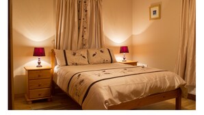 A bedroom with a wooden bed, two bedside tables with lamps, a nightstand, and a framed picture on the wall. - Beachview Cottage (Ballymena)