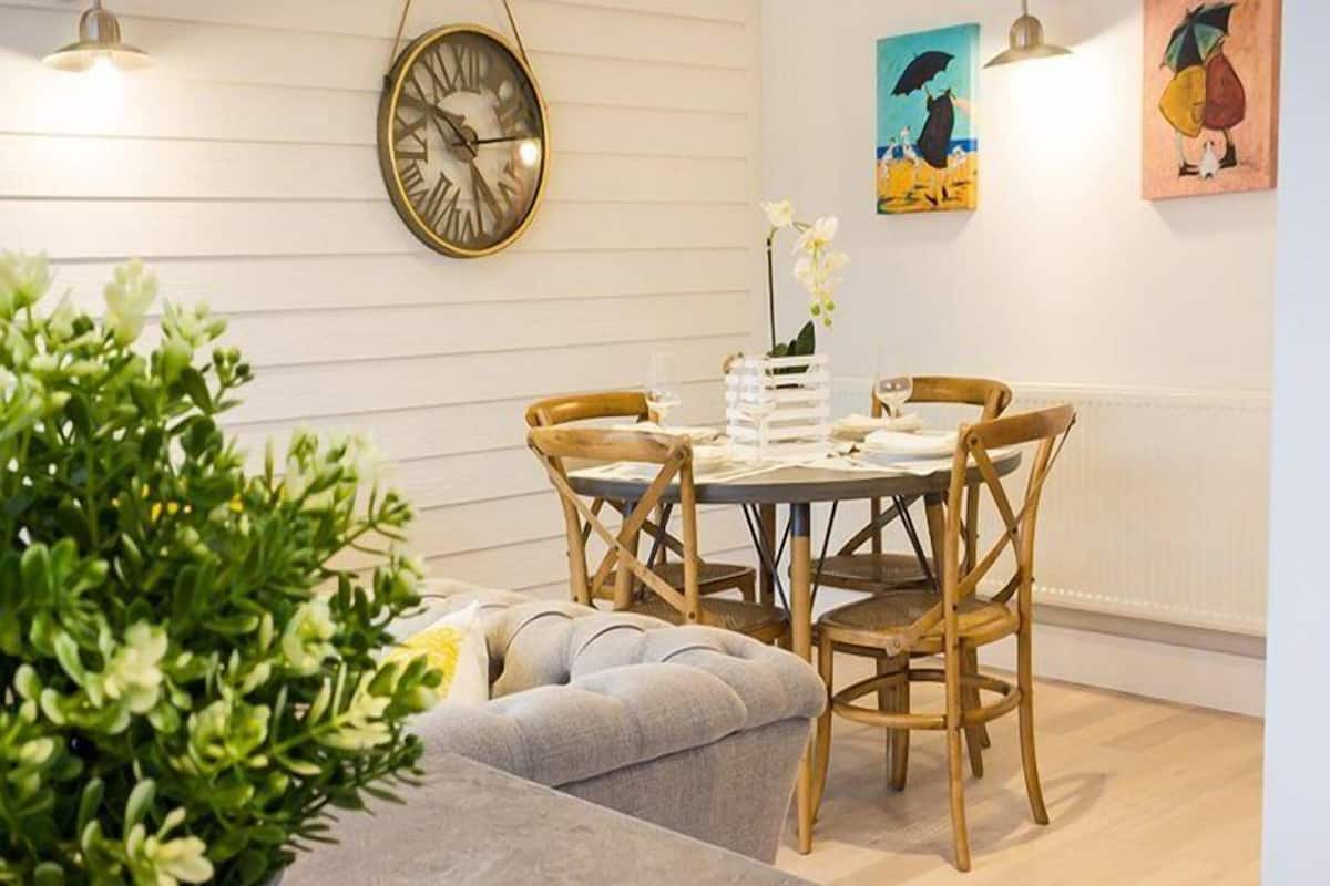 A dining area with a round table, wooden chairs, and a wall-mounted clock.