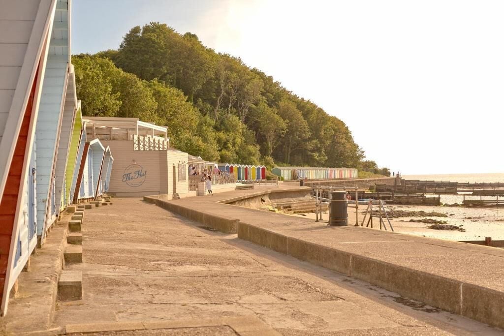 A seaside promenade with a row of colorful beach huts, a wooden structure labeled 'The Hut', and a beach in the background.