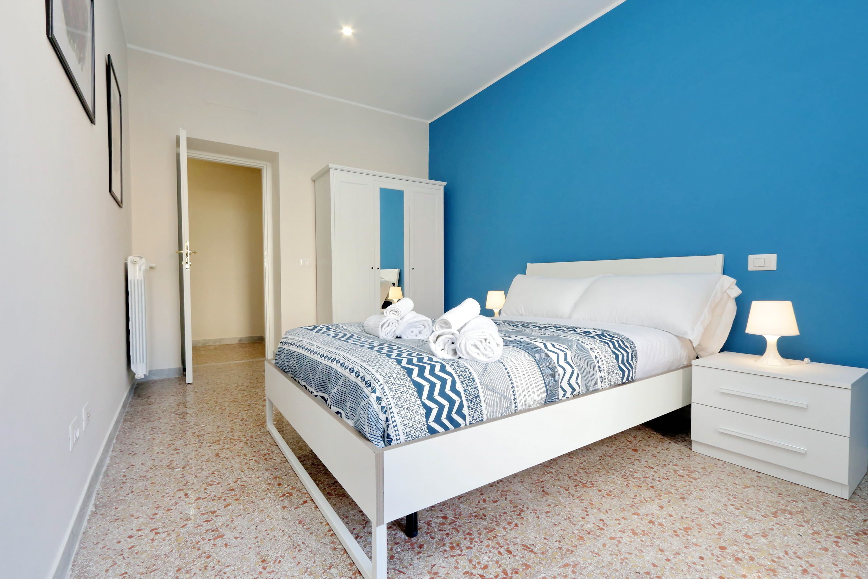 Een slaapkamer met een bed, nachtkastje, kledingkast en een deur naar een andere kamer.