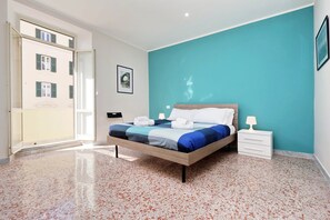 A bedroom with a bed, a nightstand, a door, and a framed picture on the wall. - Watercolors (Rome)