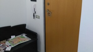 Quarto com sofá preto, porta de madeira e telefone fixado na parede.