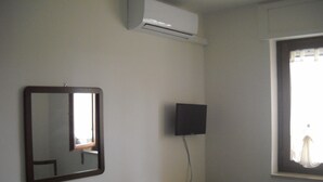 Quarto com espelho, televisão na parede, cômoda e janela com cortinas.
