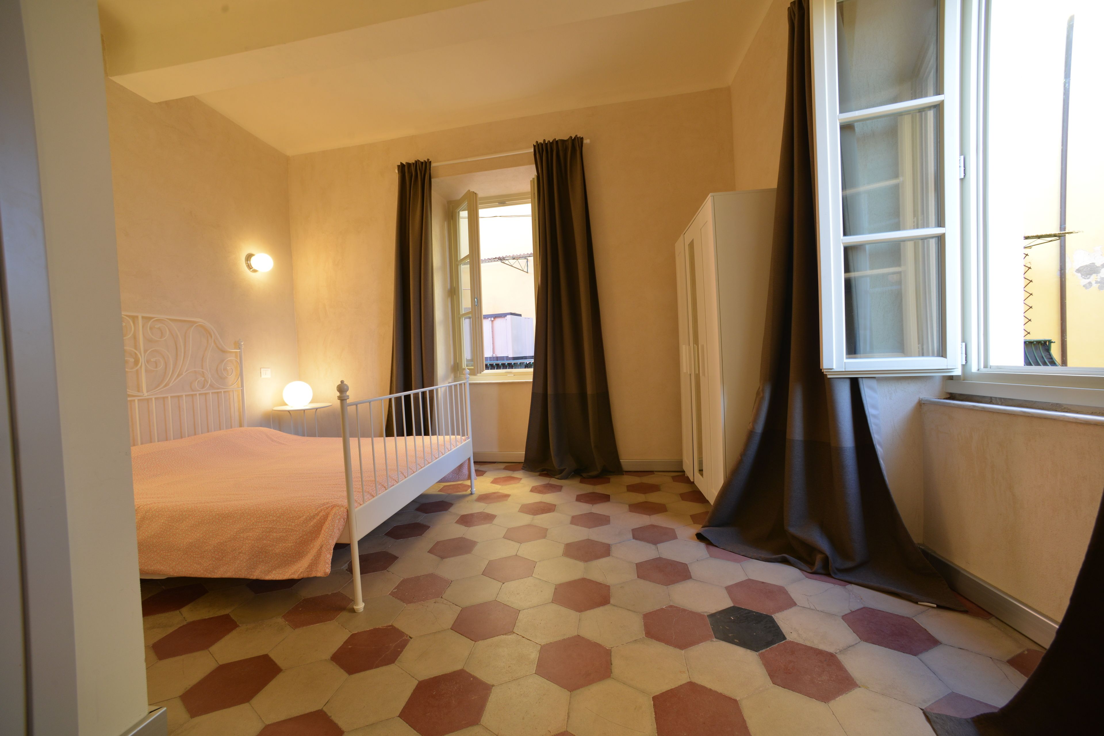 Un dormitorio con cama, ventana con cortinas, radiador y armario blanco.
