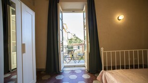 A room with a bed, a door leading to a balcony, and a hexagonal patterned floor. - Ostello Palazzo Nizza (Massa)