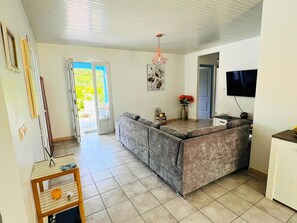 A modern kitchen with a grey sofa, a TV, and a dining area. - The Villa Passiflora (Le Diamant)