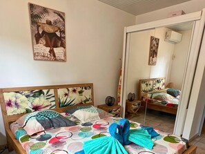 Une chambre à coucher avec un lit, une table de chevet, un miroir et un mur orné d’un tableau.