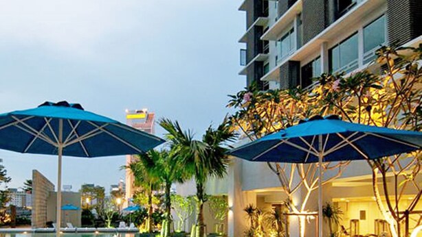 A poolside area with lounge chairs and umbrellas, surrounded by palm trees and a building with illuminated windows. - Swiss Garden Apex Suites Bukit Bintang (Kuala Lumpur)