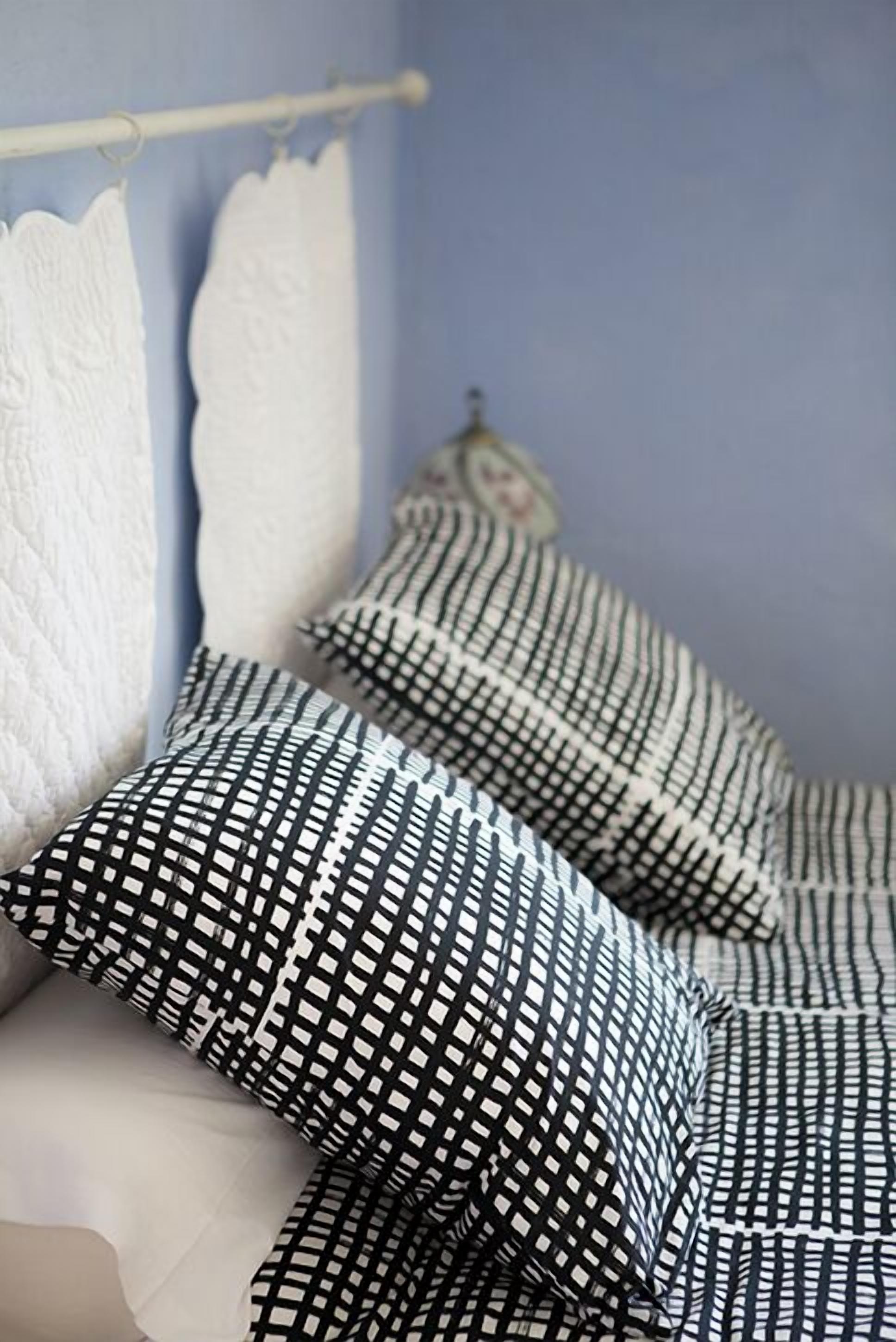 A bed with white and black patterned pillows, a white blanket, and a blue wall.