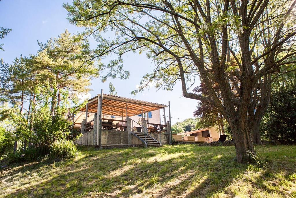 A covered outdoor area with a wooden deck, surrounded by trees and vegetation.