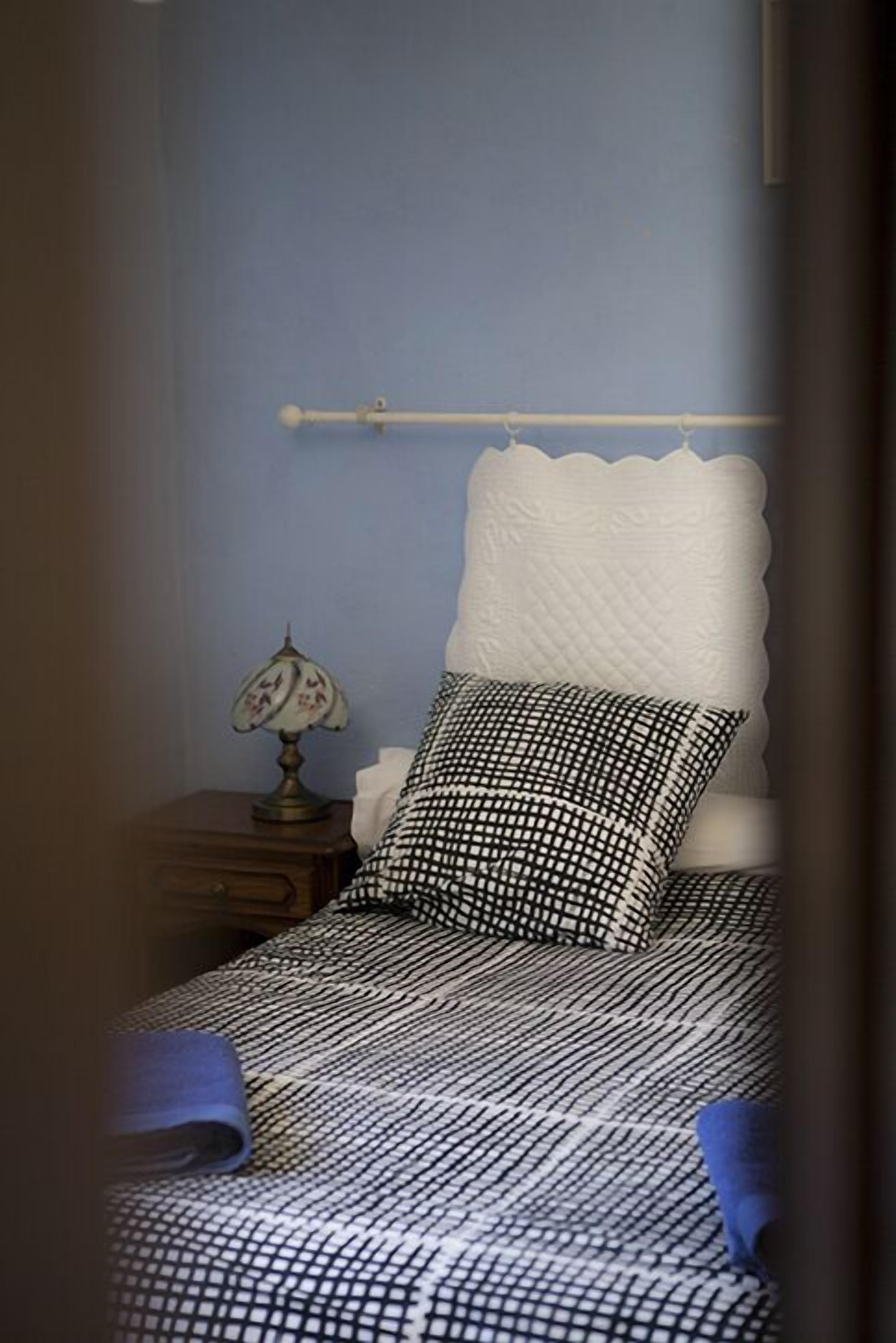 Een slaapkamer met een bed, nachtkastje, lamp en hoofdeinde.