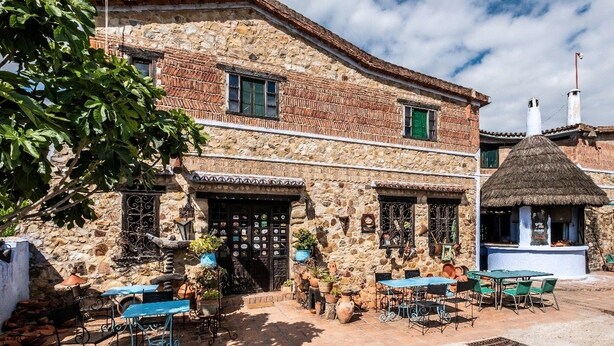 Un edificio de piedra con diseño tradicional, que presenta una estructura de techo de paja y un área de estar al aire libre.
