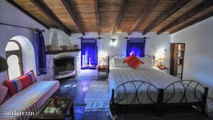 Un dormitorio rústico con chimenea de piedra, una cama con estructura de metal y un sofá con cojines a rayas.