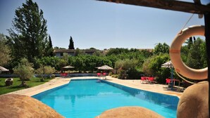 Una piscina con sillas y sombrillas rojas, rodeada de vegetación y edificios.