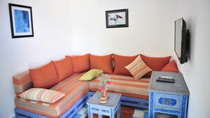 Una sala de estar con un sofá, una mesita con un jarrón y un televisor montado en la pared.